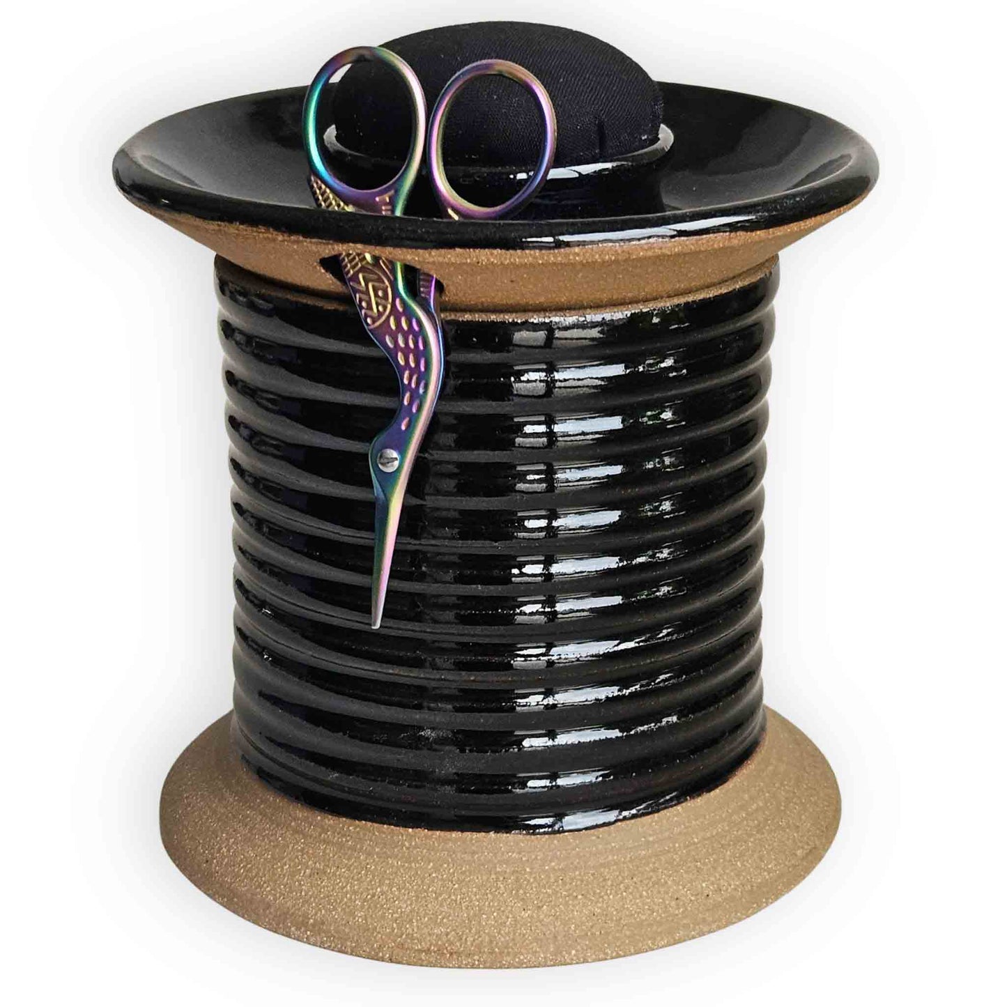 Black ceramic sewing station caddy shaped like an oversized spool with plain black pincushion topper, rainbow crane thread snips with built-in compartments for embroidery sewing and quilting supplies.