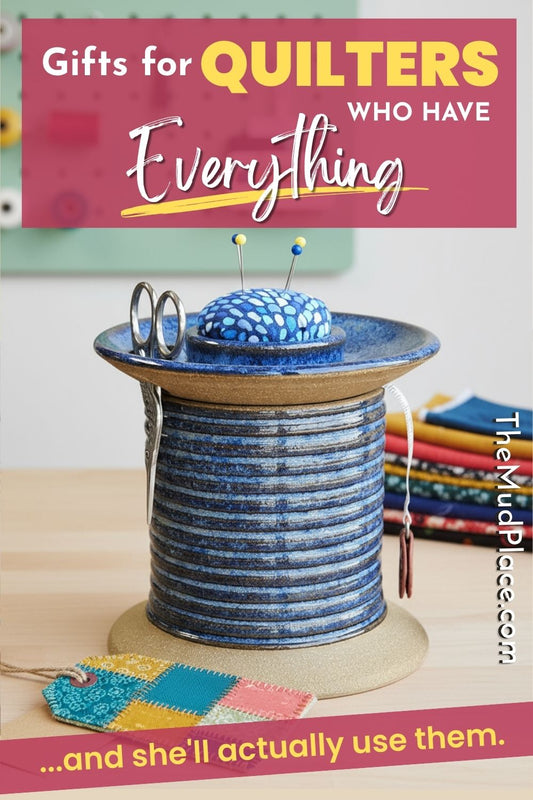 Handmade blue sewing organizer with a pincushion, scissors, and measuring tape on a sewing table beside colorful quilt fabric. Text overlay says, "Gifts for Quilters Who Have Everything... and she'll actually use them."