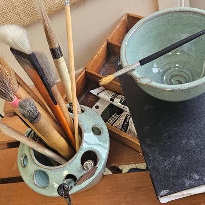 Top view of set of brushes in a ceramic holder with a wooden stand and paint supplies.