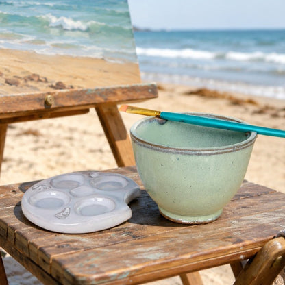 brush rinse bowl with paintbrush and ceramic palette in beach painting en plein air scene