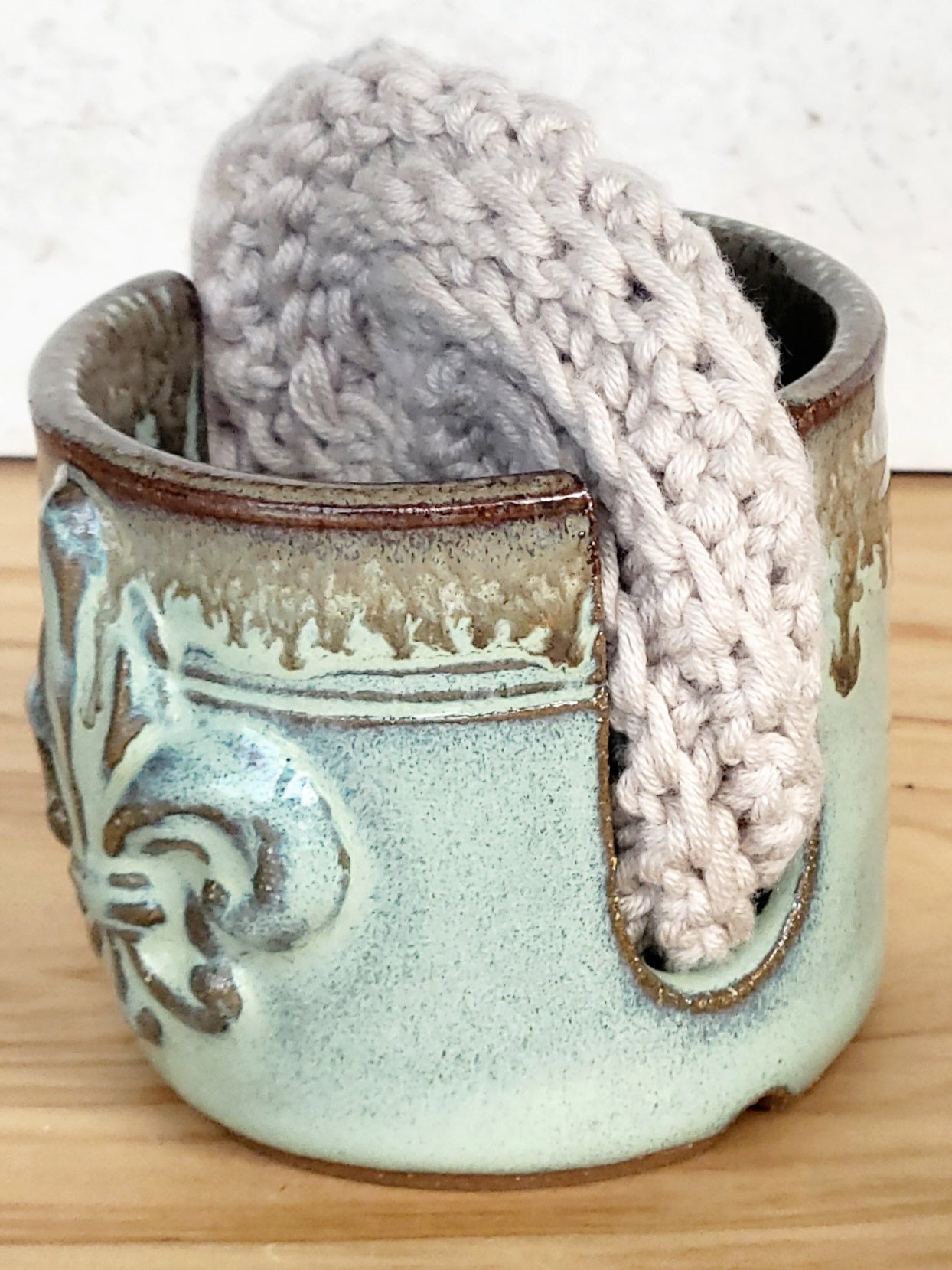 side view of ceramic green sponge keeper with a decorative fleur-de-lis design holding a crochet cotton yarn scrubber sponge. Perfect for kitchen counter organization. 