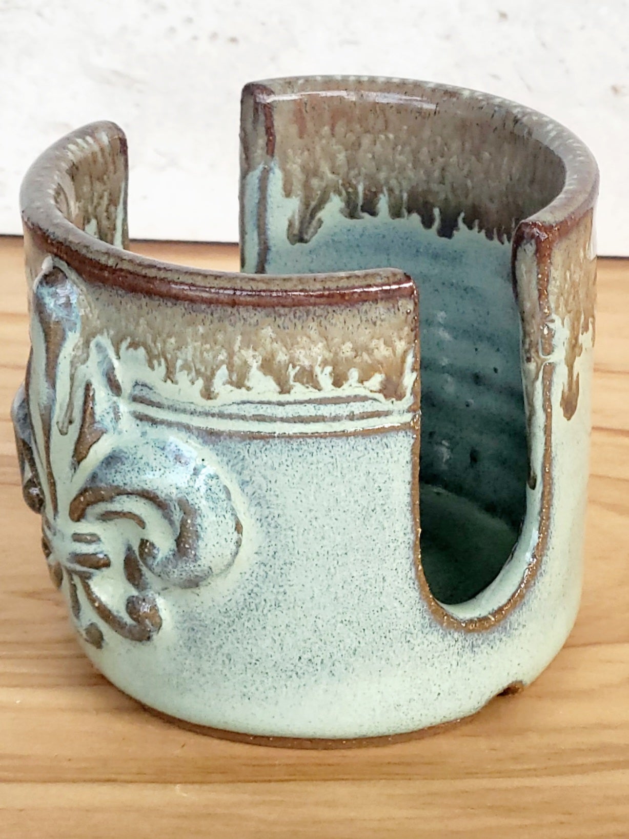 side view of ceramic green sponge keeper with a decorative fleur-de-lis design holding a crochet cotton yarn scrubber sponge. Eco-friendly kitchen countertop accessory.