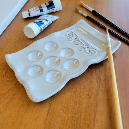 Handmade Painters palette in white ceramic with paint brush resting on it and tubes of paint ready for canvas