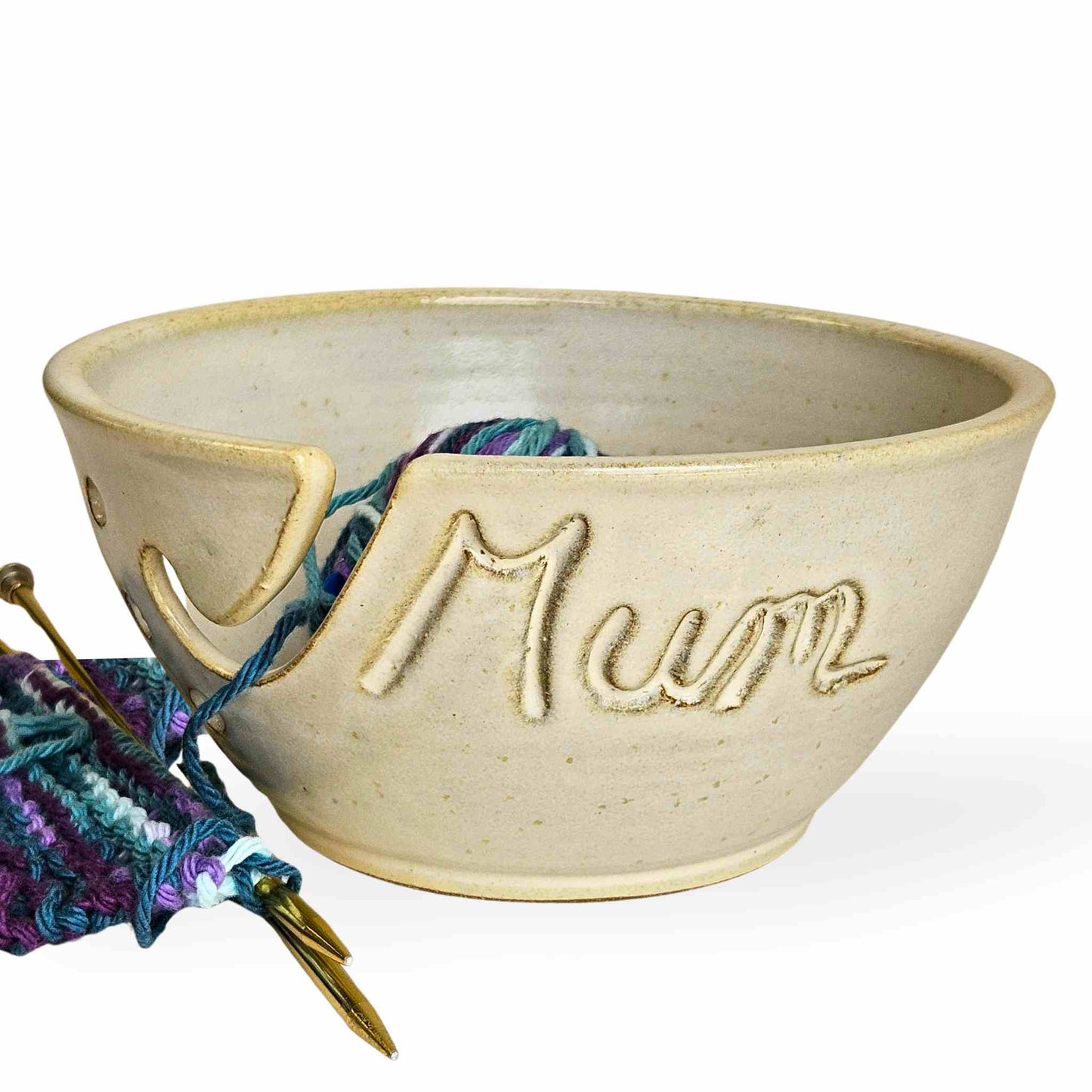 Custom yellow ceramic yarn bowl with hand-carved name “Mum” featuring a yarn guide slot and needle holes—handmade pottery gift for knitters and crocheters.
