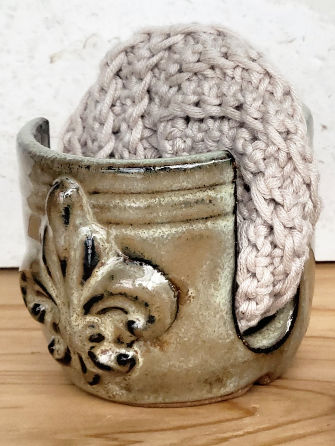 Side view of handmade artisan bronze ceramic sponge holder with embossed fleur-de-lis design, paired with a gray cotton crochet scrubber sponge. Eco-friendly kitchen countertop accessory perfect for storing crochet scrubbers, dish sponges, and sink cleaning essentials.