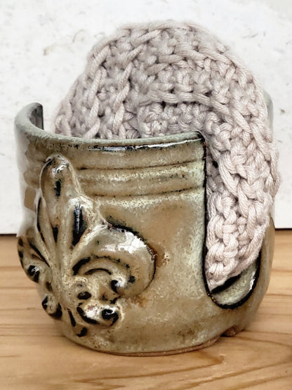 Side view of handmade artisan bronze ceramic sponge holder with embossed fleur-de-lis design, paired with a gray cotton crochet scrubber sponge. Eco-friendly kitchen countertop accessory perfect for storing crochet scrubbers, dish sponges, and sink cleaning essentials.