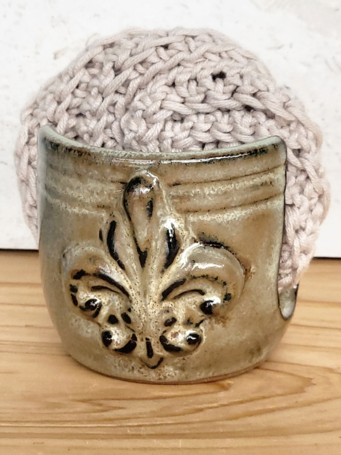 Handmade artisan bronze ceramic sponge holder with embossed fleur-de-lis design, paired with a gray cotton crochet scrubber sponge. Eco-friendly kitchen countertop accessory perfect for storing crochet scrubbers, dish sponges, and sink cleaning essentials.