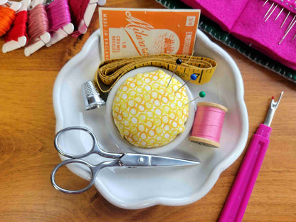 Sewing kit holder shaped like flower with scissors, thread, and pins in a pincushion on a wooden surface