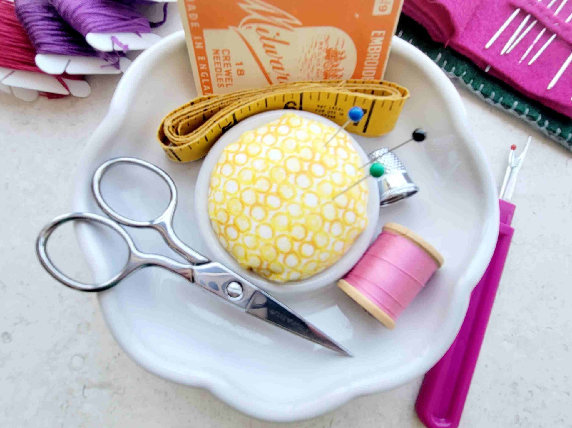 Sewing supplies including scissors, thread, and a spool of yellow thread in a white flower-shaped sewing notions holder with pincushion in center.