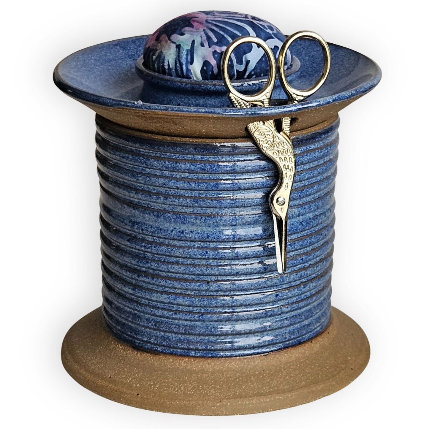 Blue ceramic sewing caddy shaped like an oversized vintage spool with batik pincushion, bobbin holder and scissor compartment with inner storage for sewing and mending supplies.