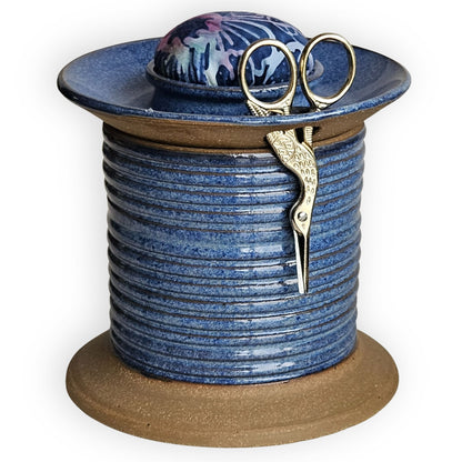 Blue ceramic sewing caddy shaped like an oversized vintage spool with batik pincushion, bobbin holder and scissor compartment with inner storage for sewing and mending supplies.