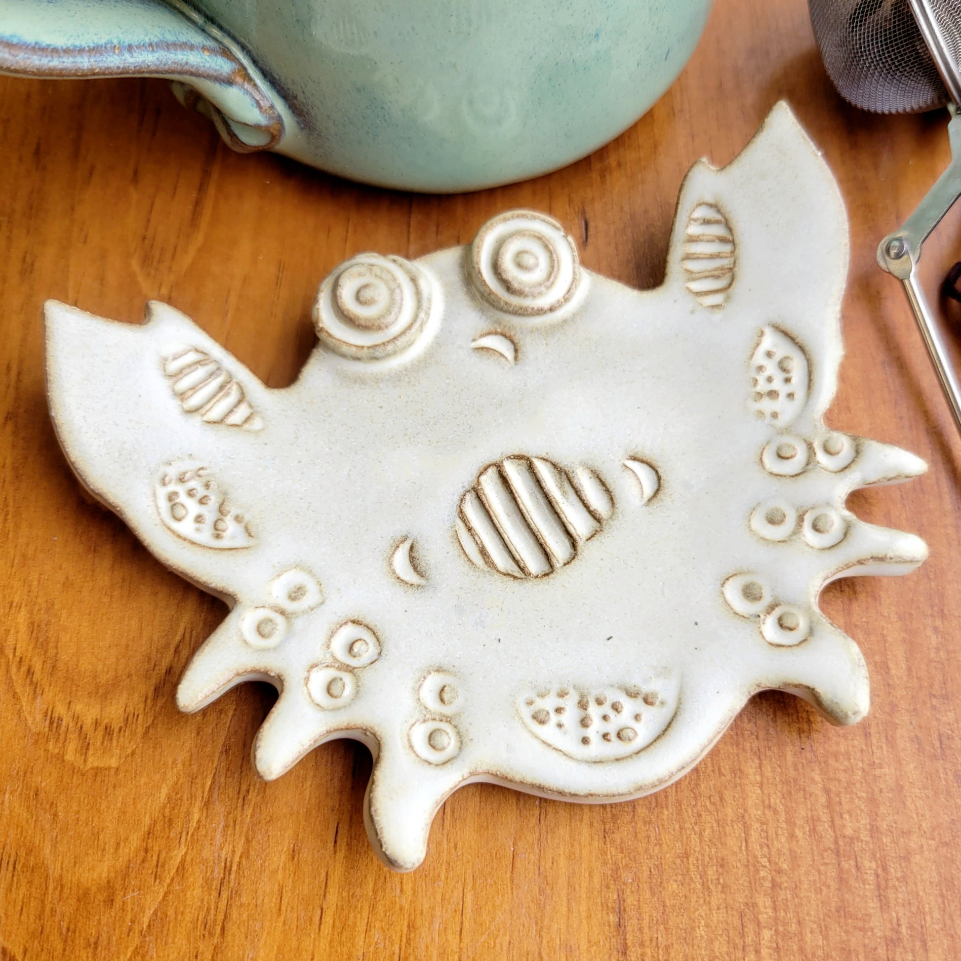 A cream-colored, crab-shaped petite spoon rest on a wooden surface.