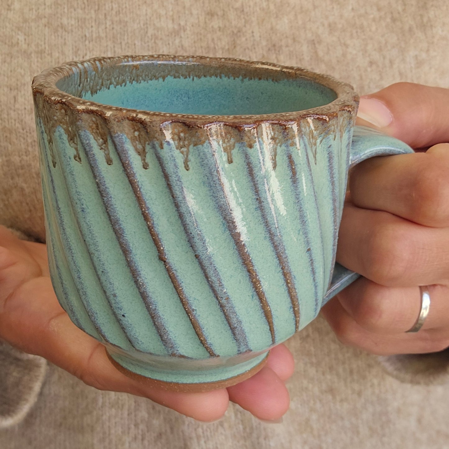 Hand holding a ceramic mug with a diagonally striped textured surface and green bronze glaze.