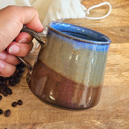 Hand holding a ceramic mug with a blue interior on a wooden surface with coffee beans.