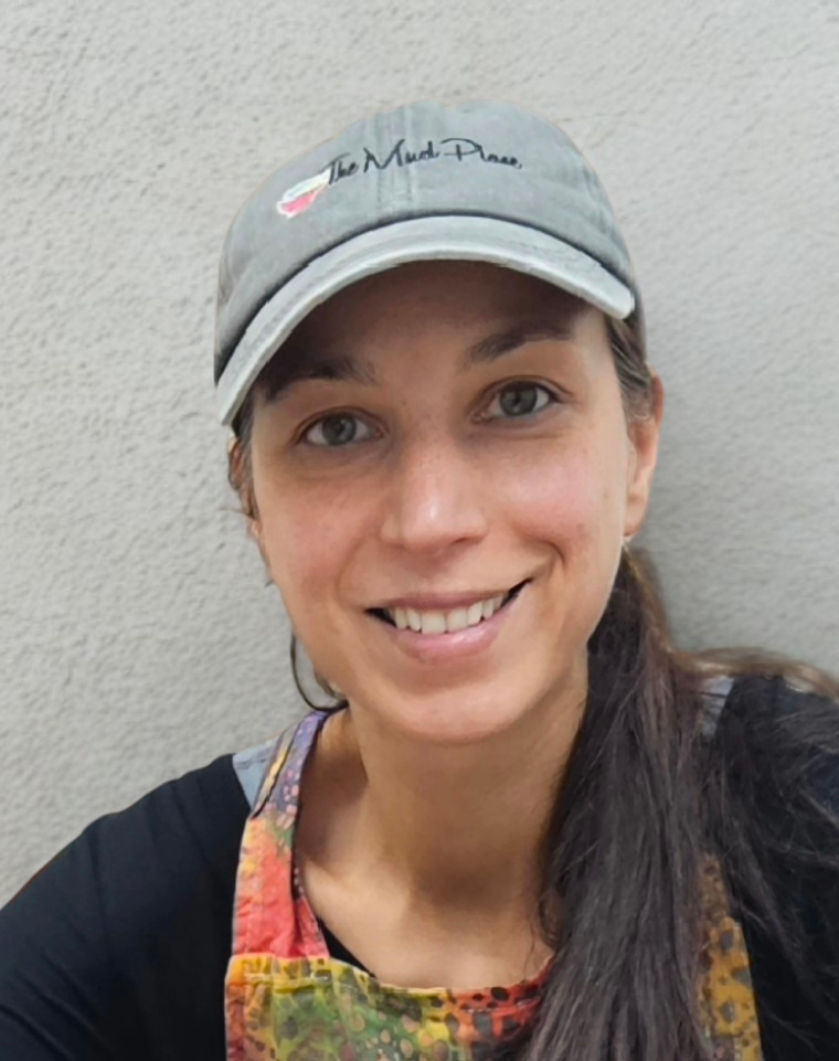 Leslie founder of The Mud Place holding her invention the Sewing Station Caddy with pins needles and scissors and she is wearing a tape measure and smiling