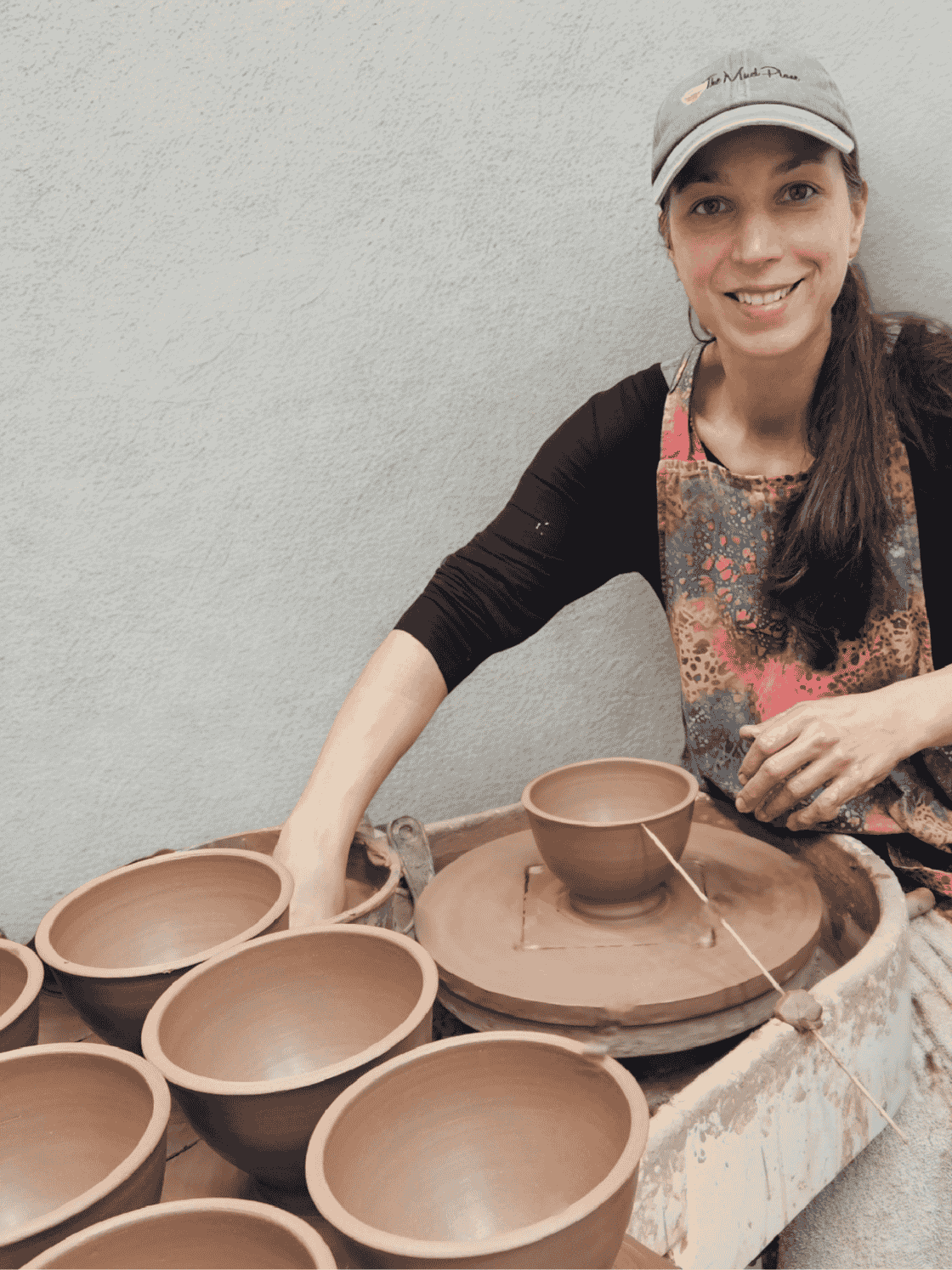 Leslie from The Mud Place working with clay pots on a pottery wheel against a plain background in her Melbourne FL Studio.