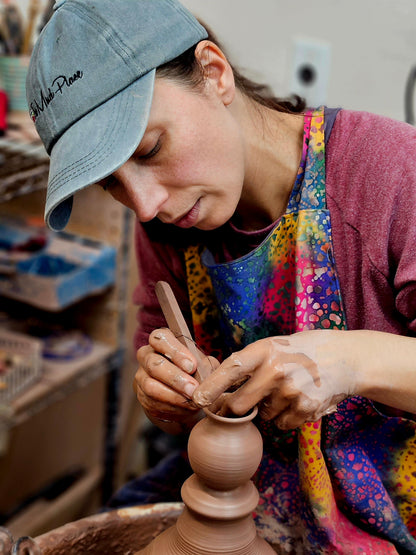 woman woring in a potter's wheel making tiny vases with small wooden tools