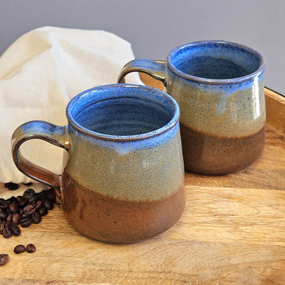set of two mugs in rust brown bronze and blue tones on a wooden tray with coffee beans in a natural cotton canvas bag 
