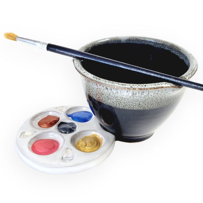 Black ceramic paint brush rinse bowl with a paintbrush holder and paint color palette on a white background