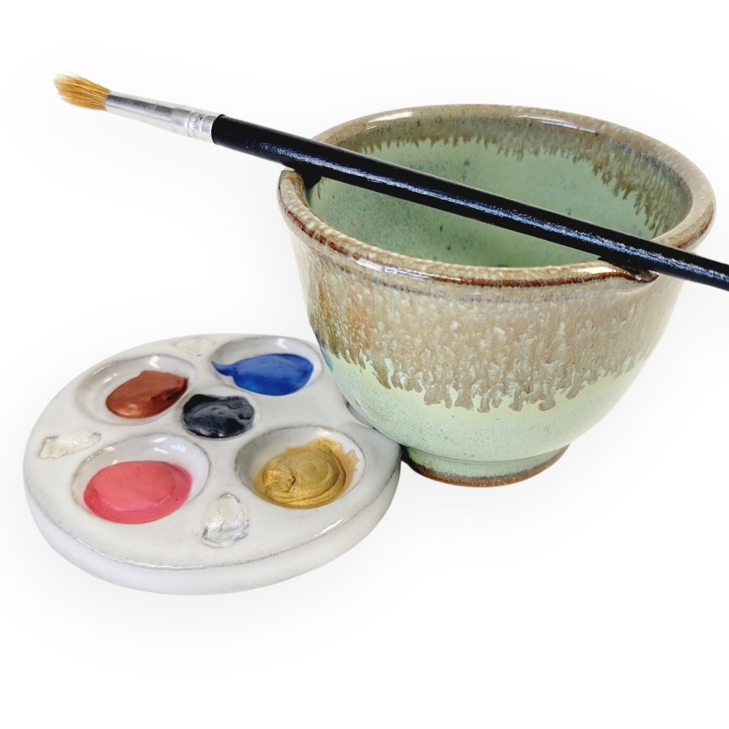 Compact green and bronze ceramic paint palette and brush rinse bowl set with textured wells and built-in brush rest holding blobs of paint and a brush in green and brown glaze.