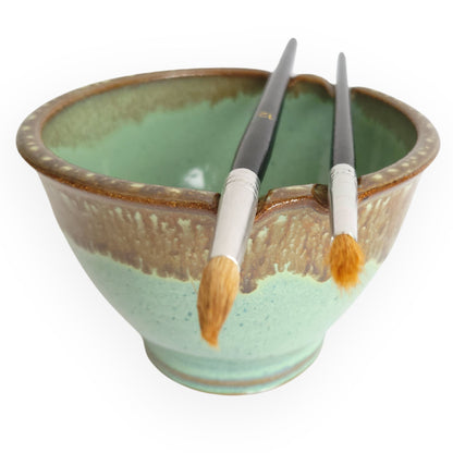 Ceramic Paint brush rinse cup with paint brushes resting in their slots on the rim in Green and Bronze.