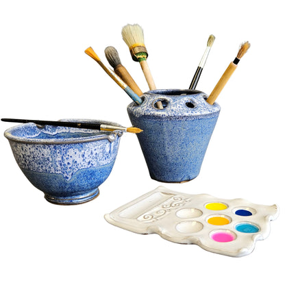 Handmade three-piece blue and white speckled ceramic artist set featuring a rinse bowl with brush rest, a matching brush holder filled with paintbrushes, and a white ceramic paint palette with colorful paints.