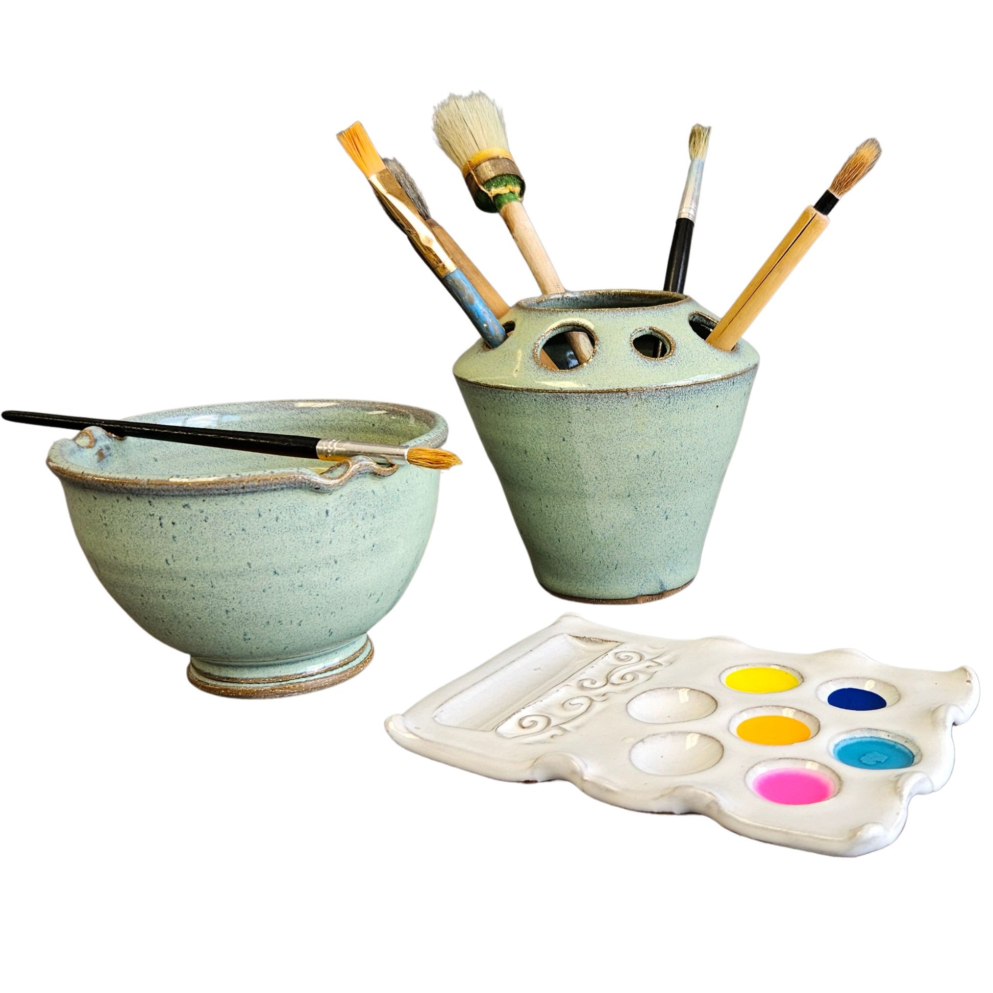 Handmade three-piece green and white ceramic artist set featuring a rinse bowl with brush rest, a matching brush holder filled with paintbrushes, and a white ceramic paint palette with colorful paints.