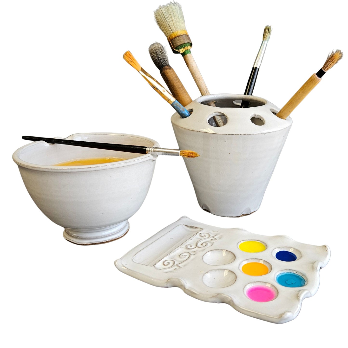 Set of handmade ceramic painting tools including a paint rinse bowl, brush organizer caddy, and a palette with colors on a white background.