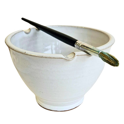 White ceramic watercolor rinse cup  with paint brush rests in rim holding a paintbrush on a white background