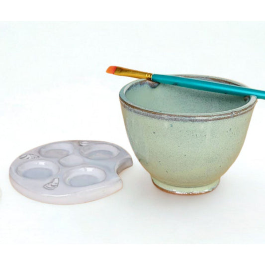Ceramic painters rinse bowl with paintbrush rest next to white palette on a white background