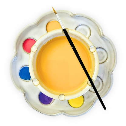 top view of a flower shaped paint palette and rinse bowl holding bright paints in 8 wells and a paint brush resting on top of the water rinse bowl