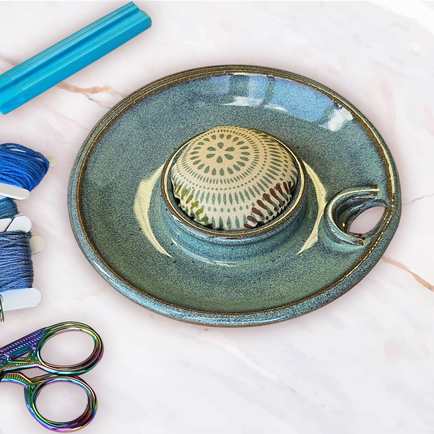 A top view of the sewing caddy lid showing the pincushion topper and scissor slot plus bobbin storage in green with scissors and embroidery floss bobbins on a table