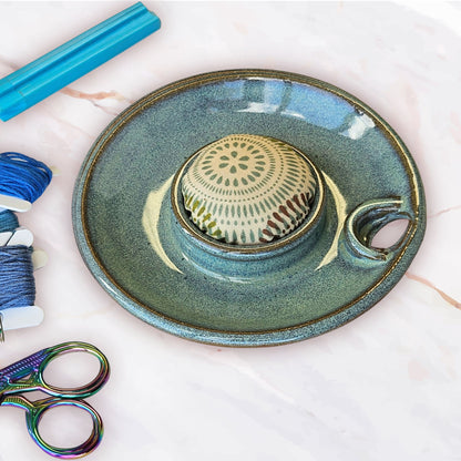 A top view of the sewing caddy lid showing the pincushion topper and scissor slot plus bobbin storage in green with scissors and embroidery floss bobbins on a table
