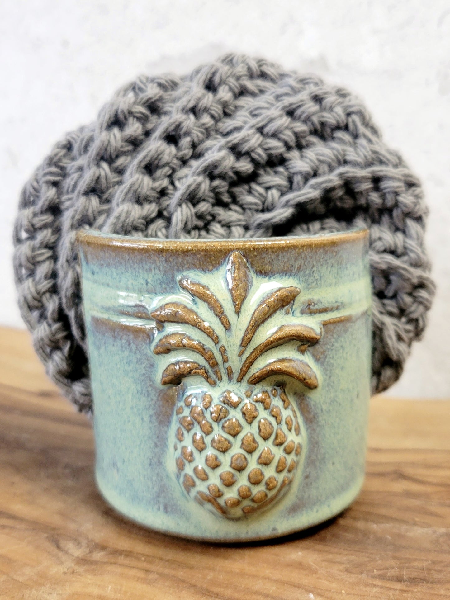 Handmade artisan green ceramic sponge holder with embossed pineapple, paired with a gray cotton crochet scrubber sponge. Eco-friendly kitchen countertop accessory perfect for storing crochet scrubbers, dish sponges, and sink cleaning essentials.