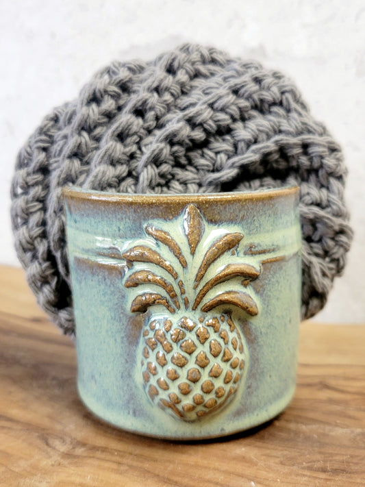 Handmade artisan green ceramic sponge holder with embossed pineapple, paired with a gray cotton crochet scrubber sponge. Eco-friendly kitchen countertop accessory perfect for storing crochet scrubbers, dish sponges, and sink cleaning essentials.