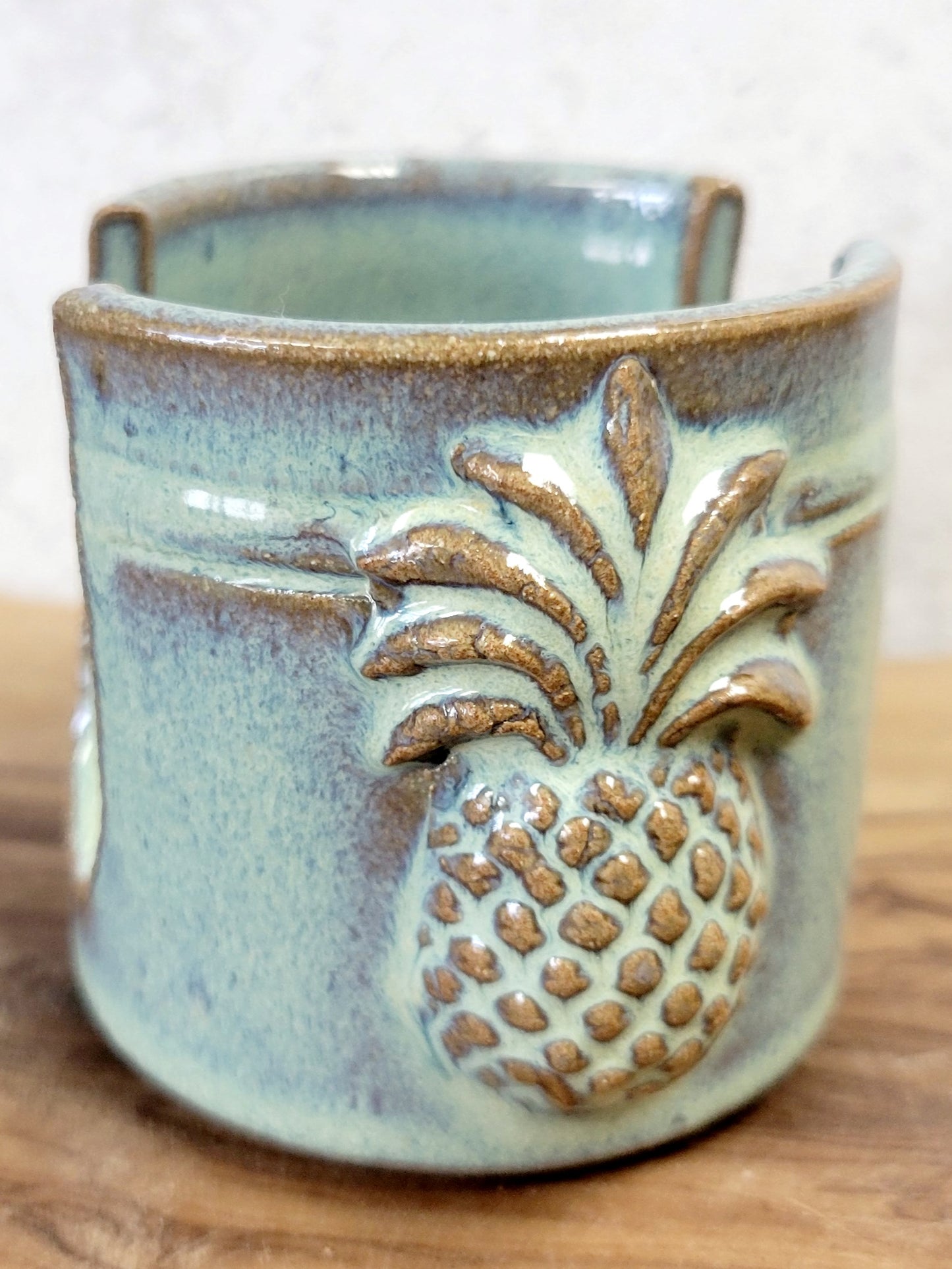 Handmade artisan green ceramic sponge holder with embossed pineapple, can hold a cotton crochet scrubber sponge. Eco-friendly kitchen countertop accessory perfect for storing crochet scrubbers, dish sponges, and sink cleaning essentials. Side view.