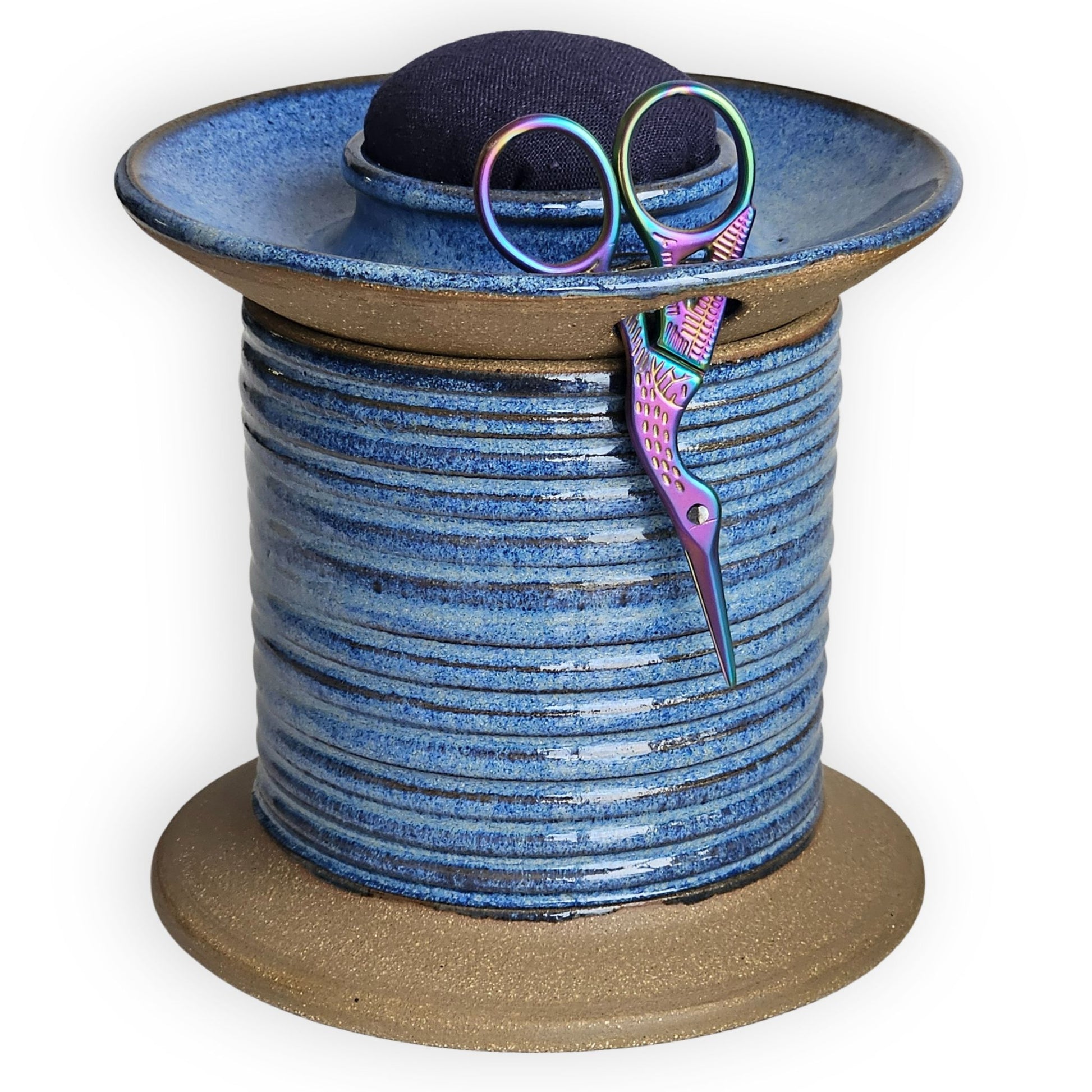 Blue ceramic sewing caddy shaped like an oversized vintage spool with navy pincushion, bobbin holder and scissor compartment with inner storage for sewing and mending supplies.