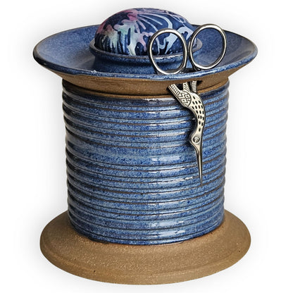 Blue ceramic sewing caddy shaped like an oversized vintage spool with batik pincushion, bobbin holder and scissor compartment with inner storage for sewing and mending supplies.