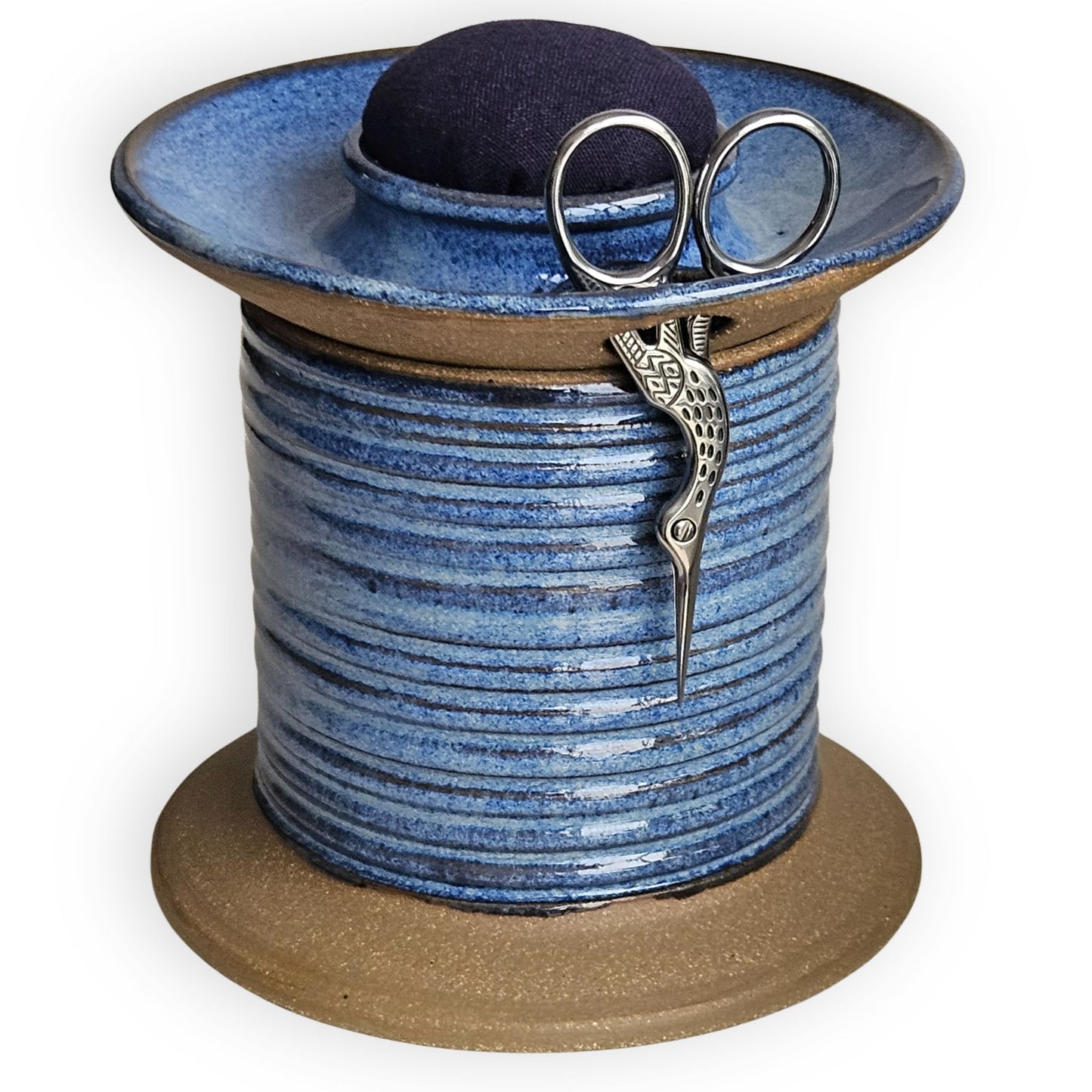 Blue ceramic sewing caddy shaped like an oversized vintage spool with navy pincushion, bobbin holder and scissor compartment with inner storage for sewing and mending supplies.