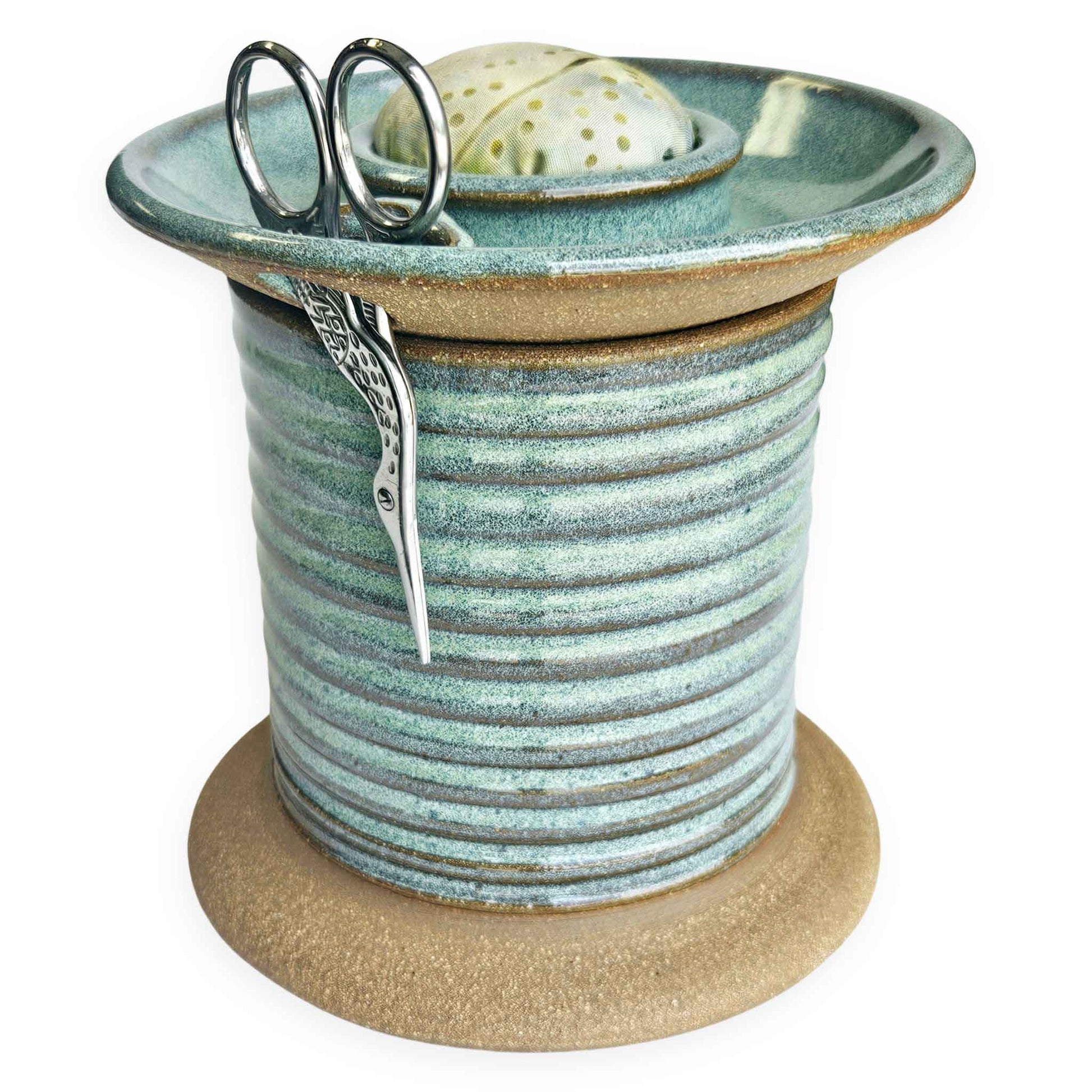 Handcrafted pottery sewing caddy designed to organize creative spaces, featuring compartments for bobbins, scissors, thread spools, and pins. This sturdy and charming piece transforms a cluttered sewing table into an inspiring, tidy workspace. A beautiful and practical gift for sewing moms, grandmothers and aunts who appreciate thoughtful, artisanal tools. The Mud Place, handmade in the USA, green, fabric pincushion