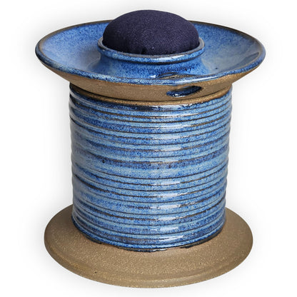 Blue ceramic sewing caddy shaped like an oversized vintage spool with navy pincushion, bobbin holder and scissor compartment with inner storage for sewing and mending supplies.