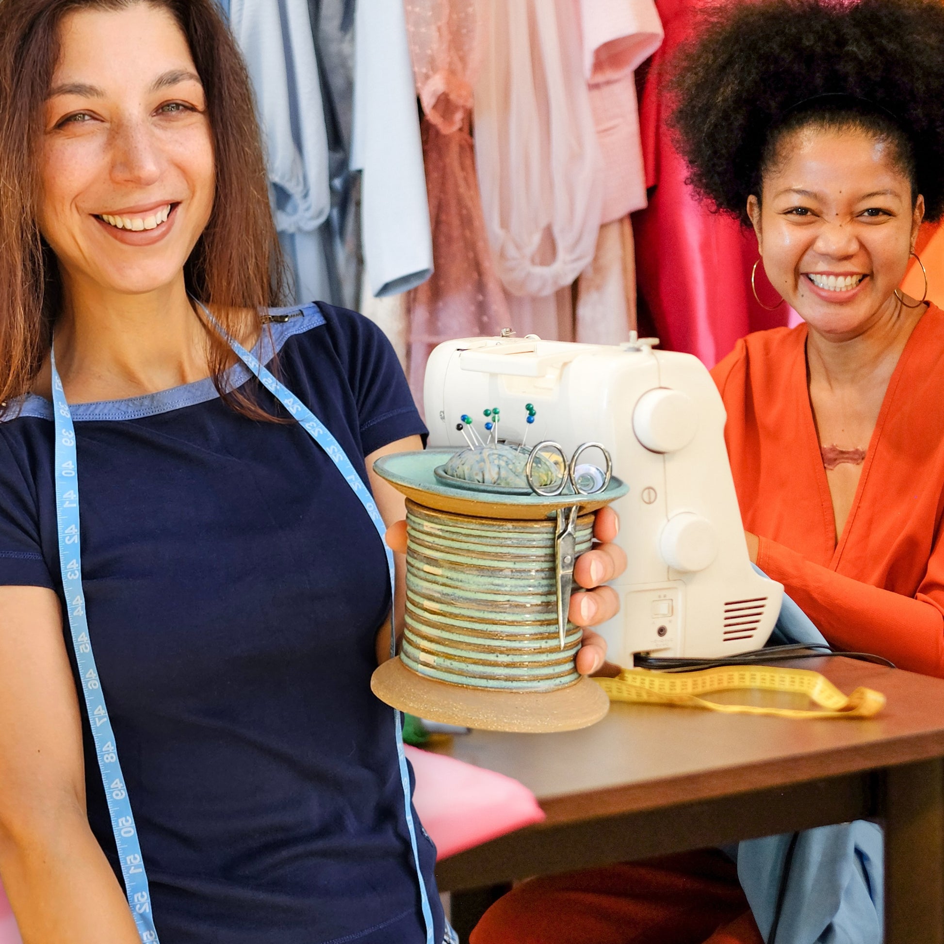 Women sewists enjoying sewing time together while holding a sewing caddy shaped like an oversized spool filled with sewing notions, pins and scissors.