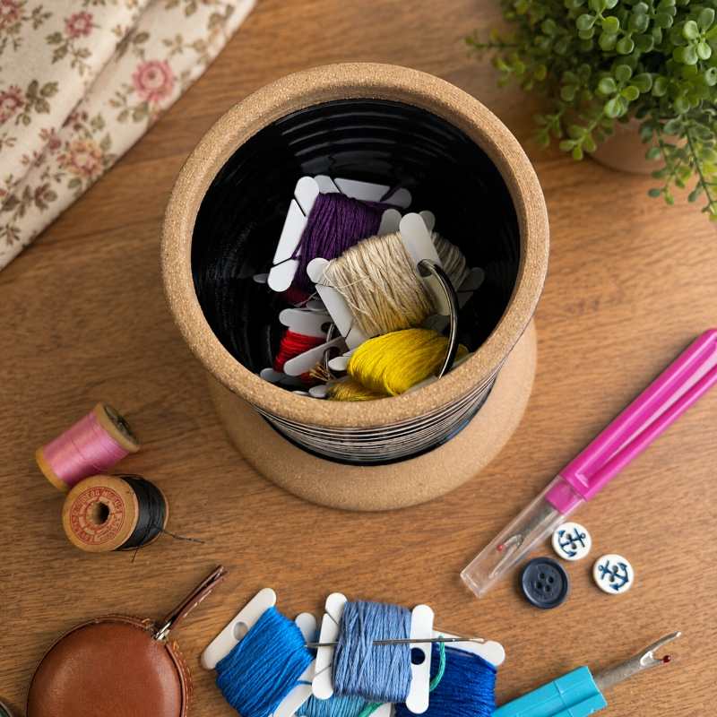 embroidery floss bobbins in a compartment with sewing notions, thread spools, seam ripper and buttons.