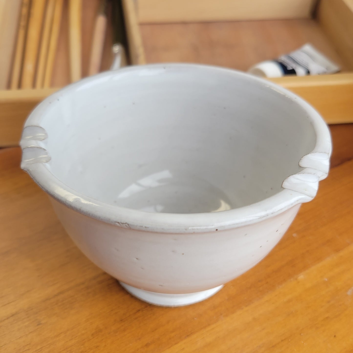 White ceramic painters rinse bowl cup with brush rest in rim on a wooden surface with painting tools in background