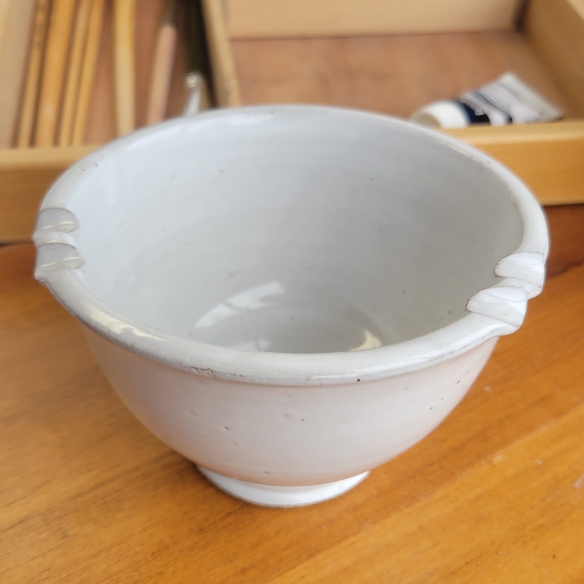 White ceramic painters rinse bowl cup with brush rest in rim on a wooden surface with painting tools in background