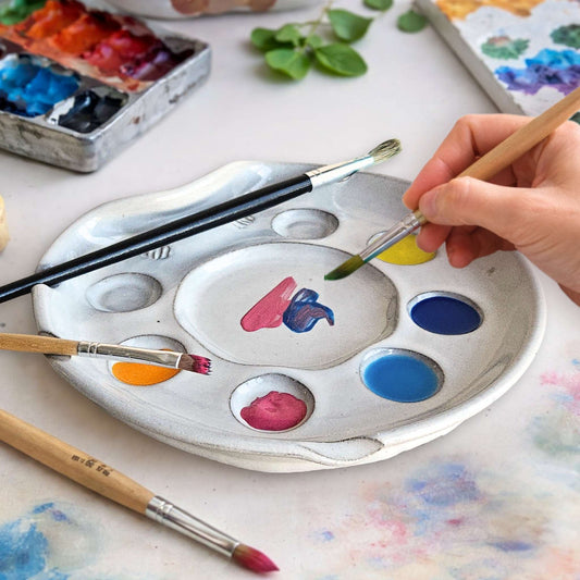 Handmade ceramic nesting artist paint palette with seven paint wells, brush rests, and center mixing well.