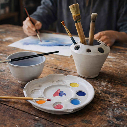 Handmade ceramic paint palette set with brush caddy and rinse bowl on a rustic table during an artist painting session.