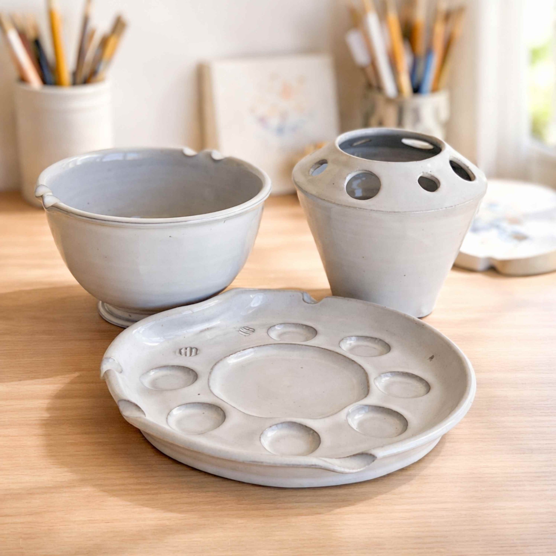 Complete handmade ceramic artist palette set including paint palette, brush holder, and rinse bowl, styled in a bright, airy studio with natural light.