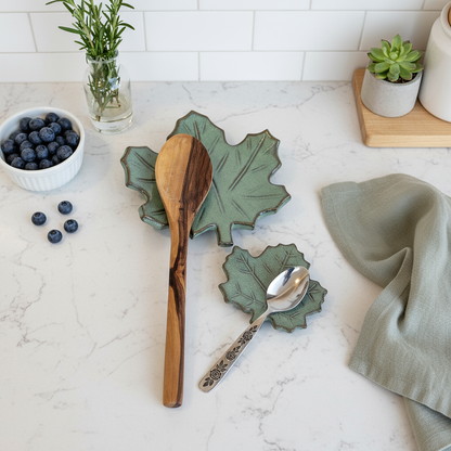 Green maple leaf spoon rest set on marble counter beside blueberries and herbs