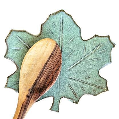 Maple leaf ceramic spoon rest in green glaze holding wooden cooking spoon